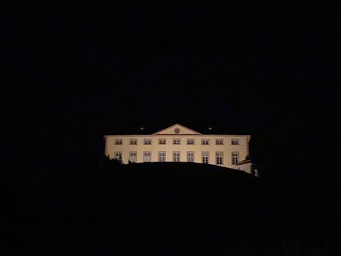 A building that is illuminated at night stands on a hill. The sky is dark and the surroundings are barely visible.