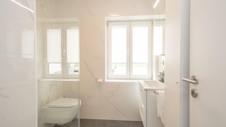 Een moderne badkamer met een glasdouche en lichte muren. Grote ramen zorgen voor veel daglicht.