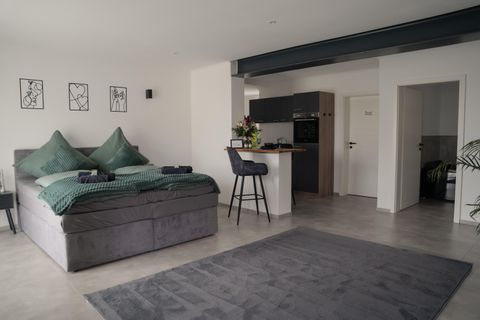 Ein modernes Schlafzimmer mit einem großen, bequemen Bett und eleganter Dekoration. An einer kleinen Bar stehen Stühle und es gibt eine gepflegte, offene Küchenzeile.