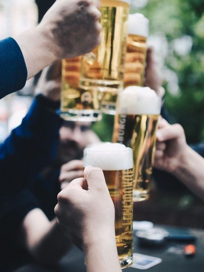 A group toast with beer glasses in a convivial gathering. The glasses are filled with golden beer and have a rich head.