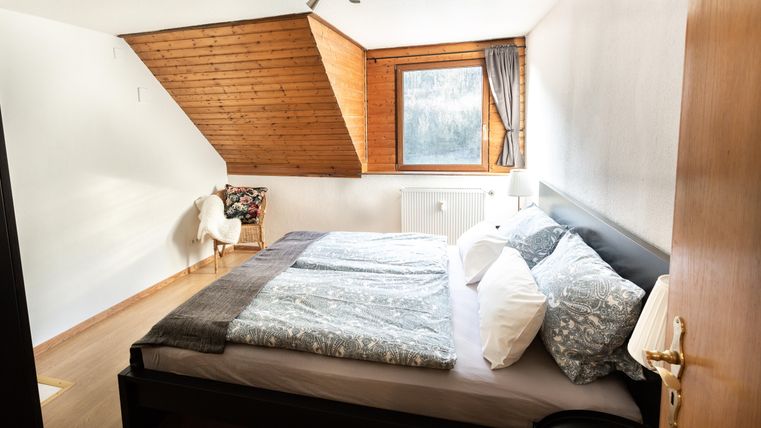 Ein gemütliches Schlafzimmer mit einem großen Bett und hellem Holzdekor. Ein Fenster bietet Tageslicht und einen Blick nach außen.