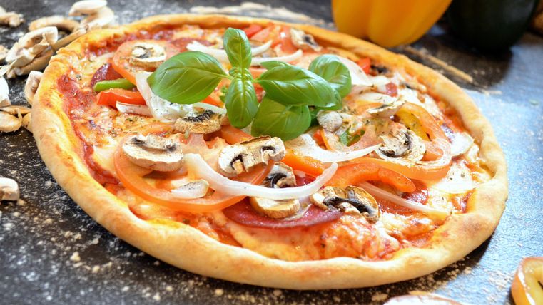 A delicious pizza with fresh vegetables and mushrooms. It is garnished with basil and has a crispy edge.