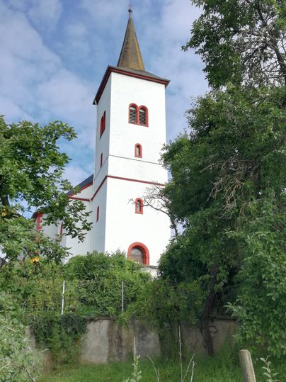 Weiße Kirche mit rotem Dach und Turm, umgeben von Bäumen.