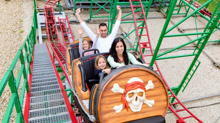 Eine Familie fährt auf einer Achterbahn mit Piratendesign. Alle haben Spaß und genießen die Fahrt.