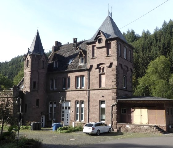 Historic red brick station building with towers, surrounded by trees and a parked car., © Eifelverein Ortsgruppe Speicher