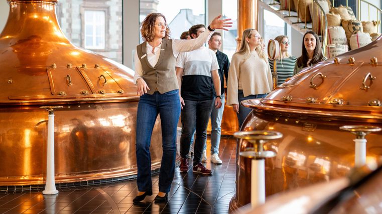 Eine Gruppe von Menschen besucht eine Brauerei. Eine Frau erklärt etwas an großen Kupferkesseln.