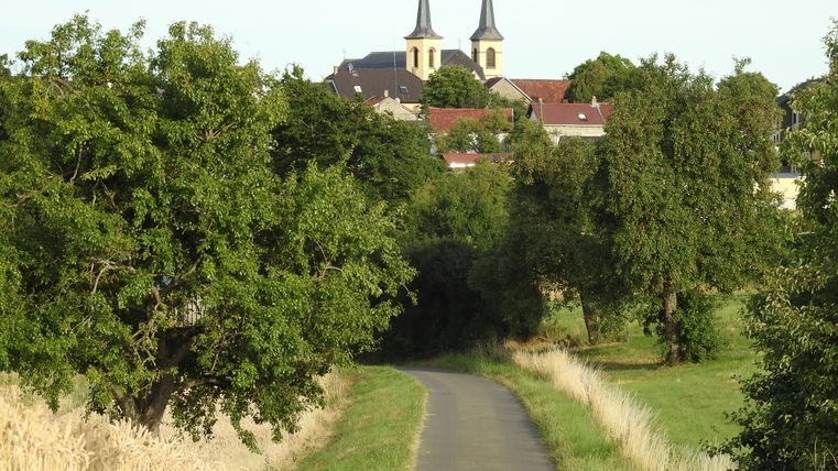 Ländliche Straße mit Bäumen und Kirche im Hintergrund in Idenheim.