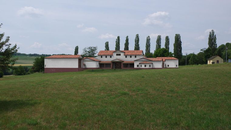 Ein großes, modernes Gebäude steht auf einer Wiesenfläche. Im Hintergrund sind hohe Bäume und ein klarer Himmel zu sehen.