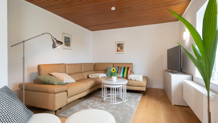 Een moderne woonkamer met een beige bank en een lage tafel. De muren zijn licht geschilderd, en een plant staat in de hoek.