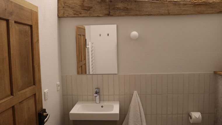 Een modern Badezimmer met een eenvoudig wasbak en een grote spiegel. De wanden zijn licht betegeld, en er is een handdoekenrek en een raam.