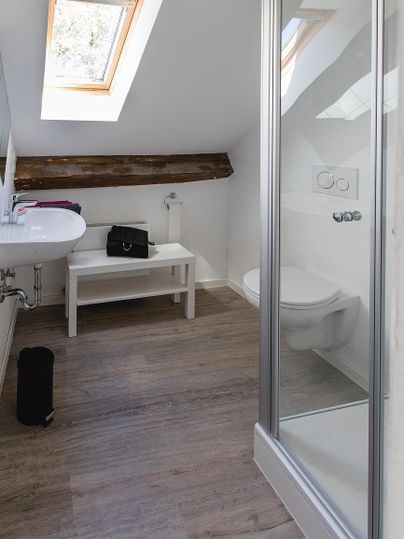 Ein modernes Badezimmer mit Dusche, Waschbecken und einem Fenstereinfall. Der Raum ist hell und freundlich, mit Holzdetails und schlichtem Design.