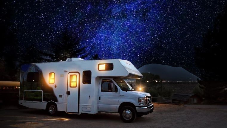Ein Wohnmobil steht unter einem klaren Sternenhimmel. Die Nacht ist dunkel und der Himmel leuchtet mit vielen Sternen.